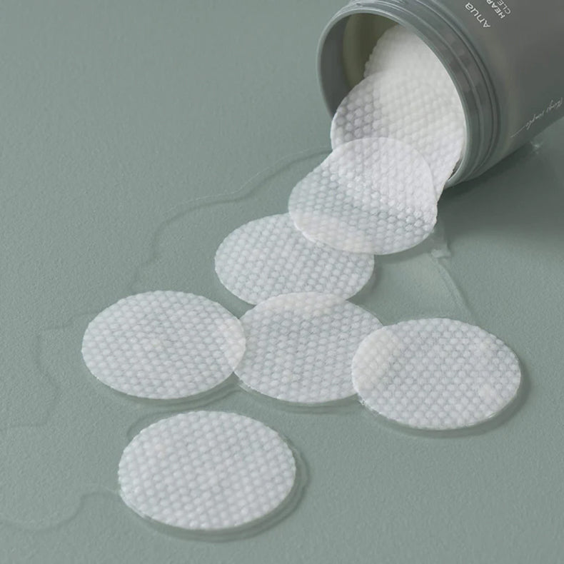 Anua Heartleaf 77% Clear Pad jar tipped over, with textured pads spilling out onto a green surface.
