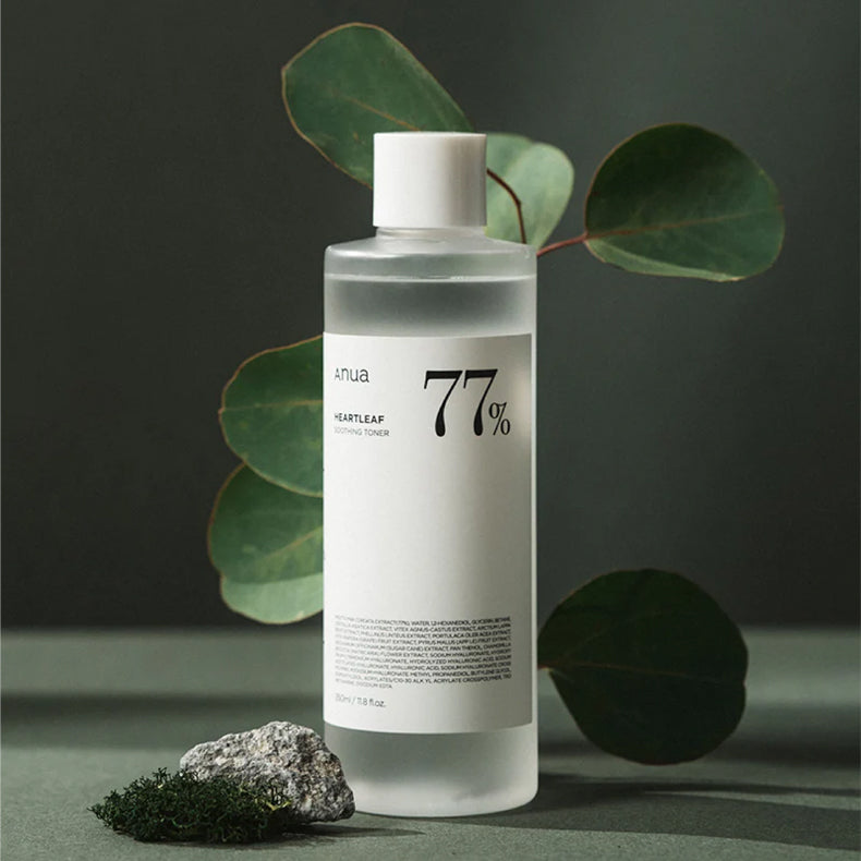 Anua Heartleaf 77% Soothing Toner bottle displayed against a dark green background with natural elements like leaves, a stone, and moss.