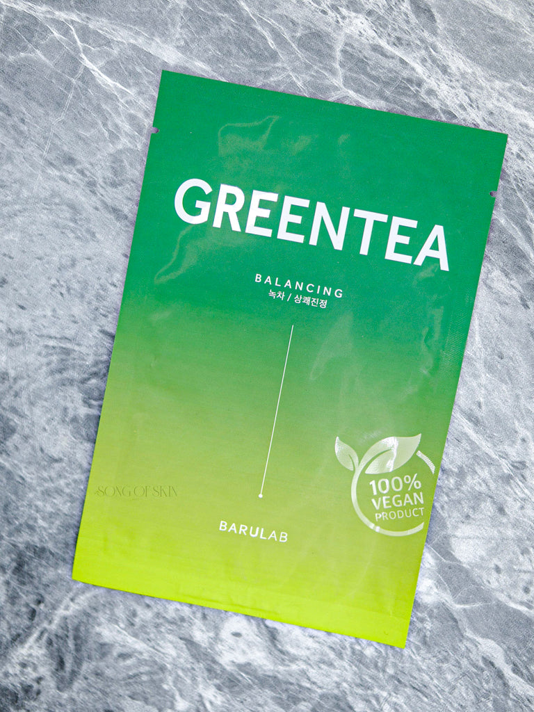 Close-up of the Barulab Clean Vegan Green Tea Mask Sheet package on a textured background resembling marble or a subtle spider web pattern.