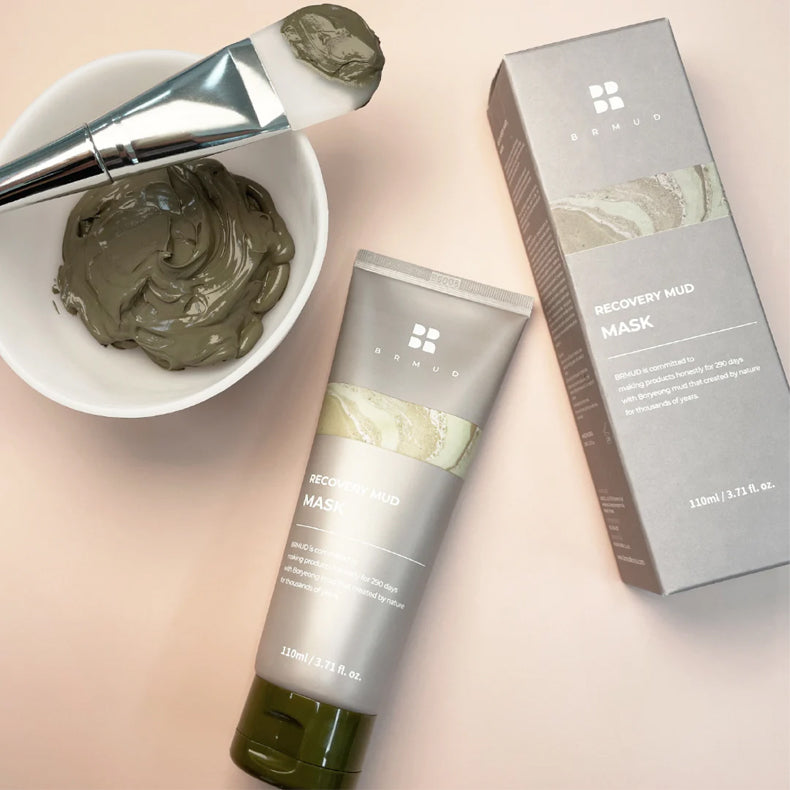 BRMUD Recovery Mud Mask tube and packaging alongside a bowl of mud mask and applicator brush.