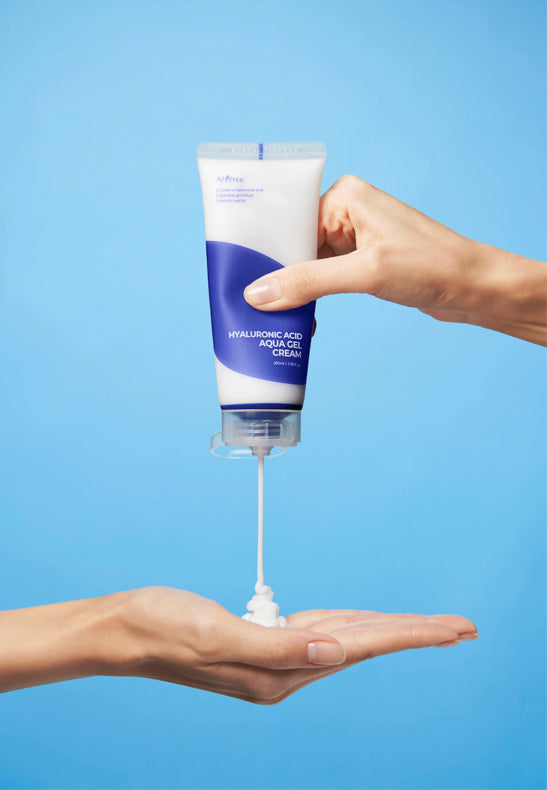 Isntree Hyaluronic Acid Aqua Gel Cream being dispensed into a hand, showing the creamy, hydrating texture against a blue background.