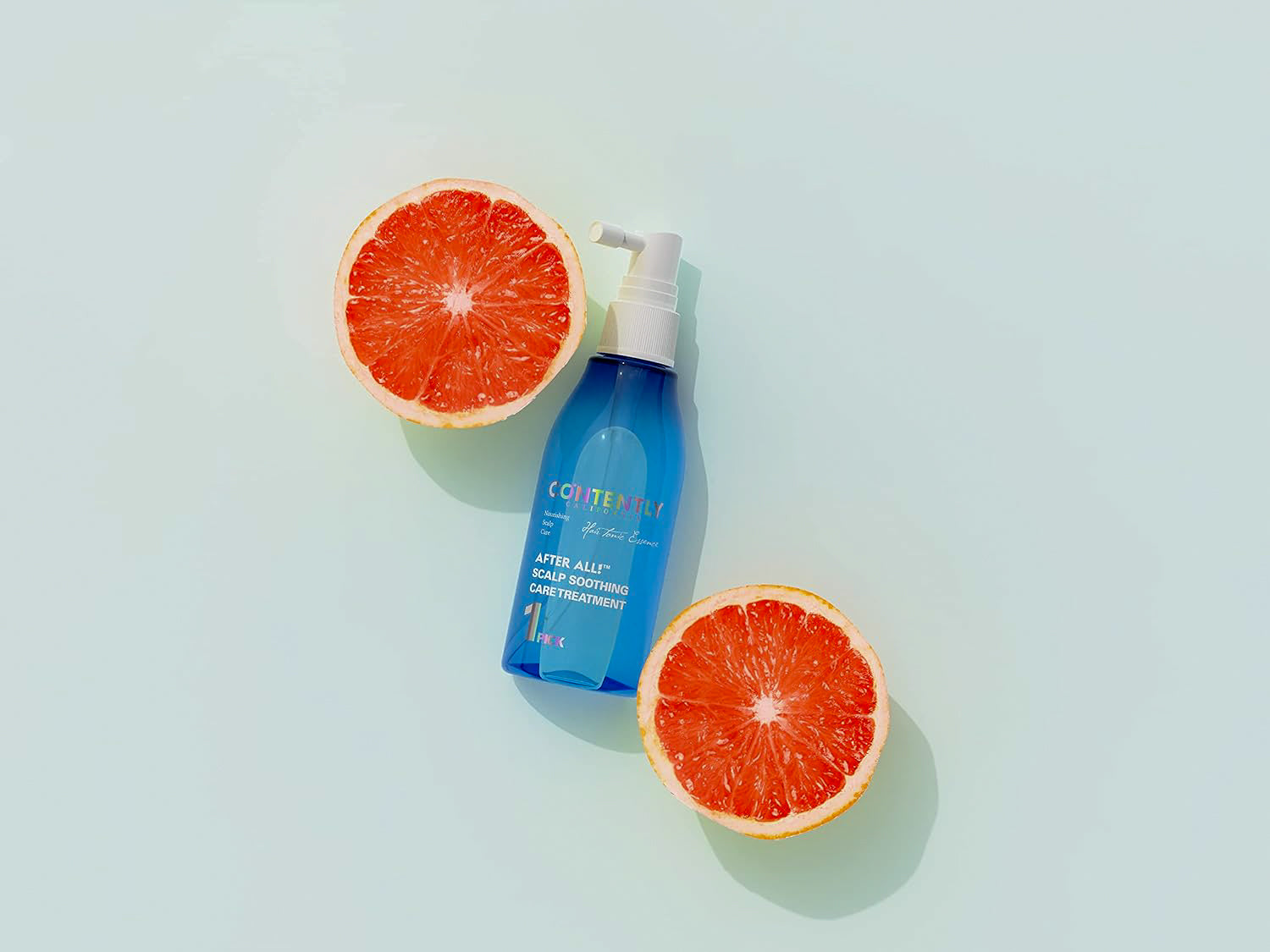 Contently After All! Scalp Soothing Care Treatment bottle displayed between two halves of a grapefruit on a light background.